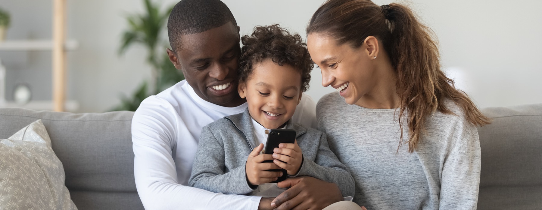 Man, woman and child sitting on couch looking at phone